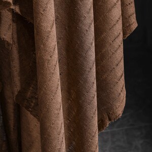 May include: Brown fabric with a textured, diagonal pattern. The fabric is folded and draped, creating a soft, flowing look.