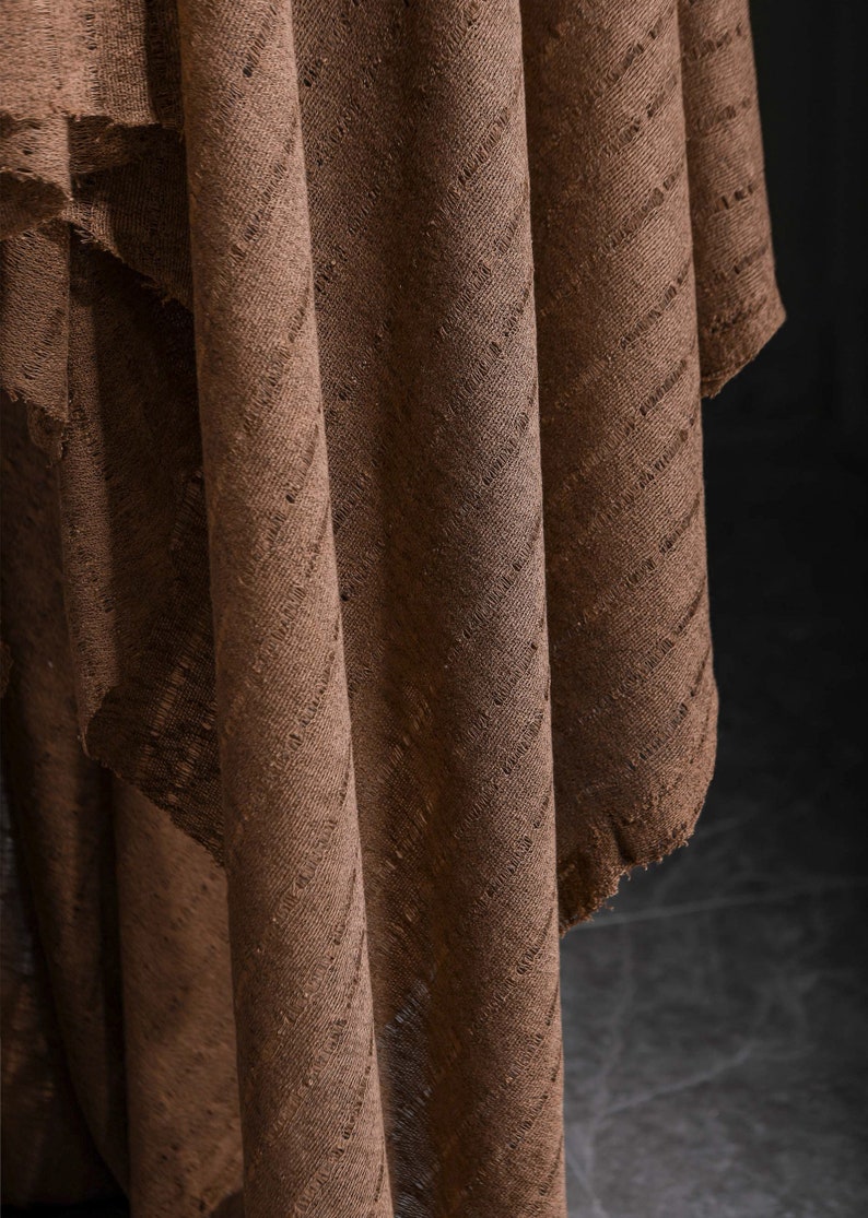 May include: Brown fabric with a textured, diagonal pattern. The fabric is folded and draped, creating a soft, flowing look.