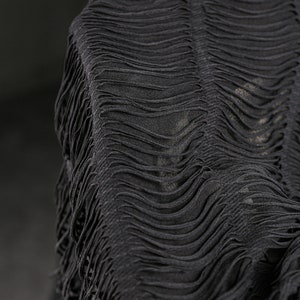 Puede incluir: Tela negra con detalle de flecos. La tela es texturizada y tiene un patr&oacute;n ondulado.