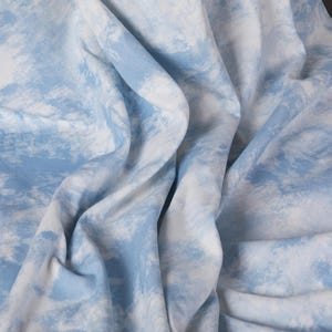 Op de afbeelding: Een blauwe en witte stof met een tie-dye patroon. De stof is zacht en heeft een licht getextureerd oppervlak.