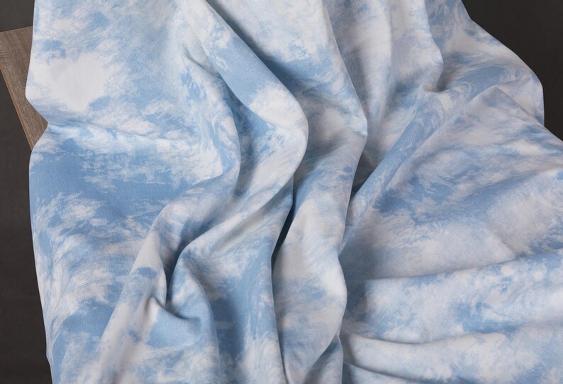Op de afbeelding: Een blauwe en witte stof met een tie-dye patroon. De stof is zacht en heeft een licht getextureerd oppervlak.