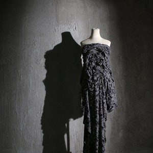 May include: A gray dress with a ruffled texture on a white mannequin against a gray concrete wall.