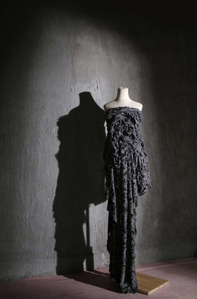May include: A gray dress with a ruffled texture on a white mannequin against a gray concrete wall.