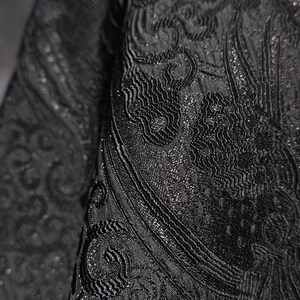 K&ouml;nnte beinhalten: Nahaufnahme eines schwarzen Stoffes mit einem komplizierten, erhabenen Paisley-Design. Der Stoff hat einen subtilen Glanz, mit einer strukturierten Oberfl&auml;che und detaillierten Mustern. Das Design ist ein sich wiederholendes Motiv, das einen luxuri&ouml;sen Look erzeugt.