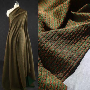 May include: A length of fabric in green and brown tones, draped over a mannequin. The material features a textured, woven design, with a detailed close-up revealing the intricate pattern. The fabric's colour scheme includes green, brown, and orange.