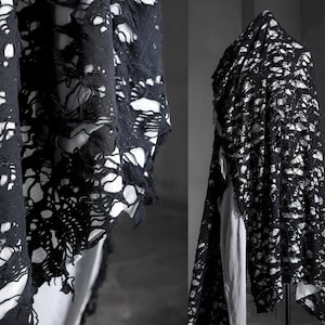 May include: Black fabric with a distressed, ripped, and torn design. The fabric has a lace-like appearance with large holes throughout. The fabric is draped over a mannequin.