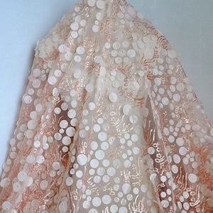 May include: A sheer fabric with a rose gold glitter background and large white 3D circles. The fabric is perfect for making dresses, skirts, and other garments.