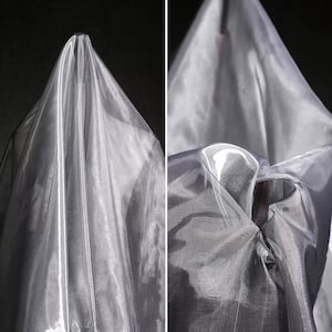 May include: Two-panel image of draped, sheer, silver fabric. The fabric is gathered and folded, creating a layered effect. The material has a subtle sheen, reflecting light and adding depth. The background is dark, emphasizing the fabric's texture and color.