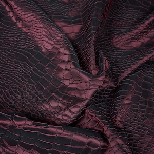 May include: Close-up of a burgundy fabric with a crocodile-embossed pattern. The fabric is wrinkled and has a shiny finish.