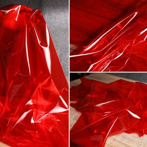 Op de afbeelding: Rode transparante plasticfolie, gevouwen en gedrapeerd op een houten oppervlak. De folie is glanzend en heeft een licht rimpel effect.