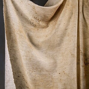 May include: A beige fabric with a textured pattern and brown spots. The fabric is draped over a hand.