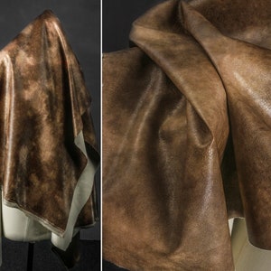 Peut inclure: Un gros plan sur un tissu en cuir brun avec un aspect marbré et vieilli. Le tissu est plié et drapé, révélant sa texture et ses variations de couleur.