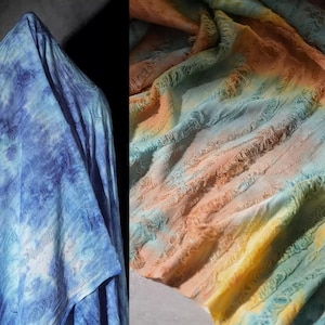 May include: Two pieces of fabric. One is a blue tie-dye pattern, the other is a colorful fabric with orange, yellow, and blue hues. The fabric has a textured, rippled appearance, with a soft, flowing drape.