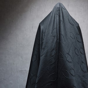 May include: A person is completely covered in a black fabric with a textured pattern. The fabric is draped over the person's head and body, obscuring their features.