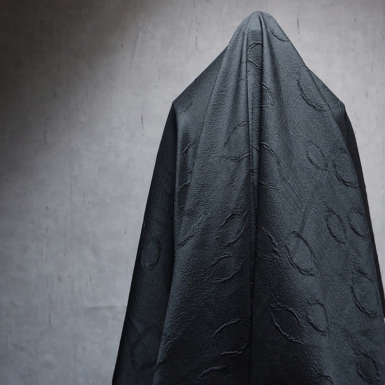 May include: A person is completely covered in a black fabric with a textured pattern. The fabric is draped over the person's head and body, obscuring their features.