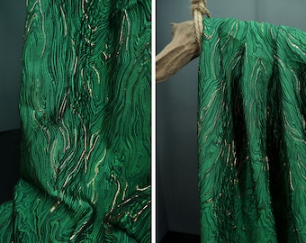 May include: Green fabric with a gold metallic swirl pattern. The fabric is draped over a wooden branch.