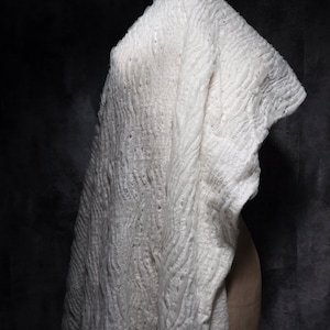 May include: White fabric with a textured, wavy pattern. The fabric is draped over a form and has a delicate, airy feel.