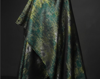May include: A green and gold fabric with a metallic sheen. The fabric has a distressed, abstract pattern.