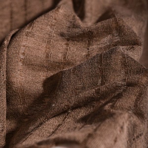 May include: Close-up of a brown fabric with a textured woven pattern. The fabric has a soft, slightly rough texture.