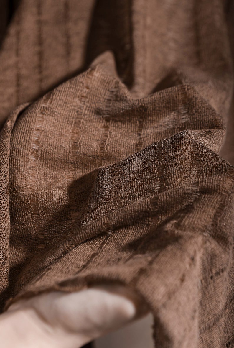 May include: Close-up of a brown fabric with a textured woven pattern. The fabric has a soft, slightly rough texture.