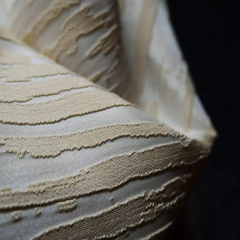 May include: Close-up of a white and beige textured fabric with a striped pattern. The fabric is soft and luxurious, with a subtle sheen.