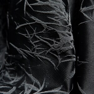 May include: Black fabric with a textured, embossed pattern of leaves and branches. The fabric has a subtle sheen and a soft, drapey feel.
