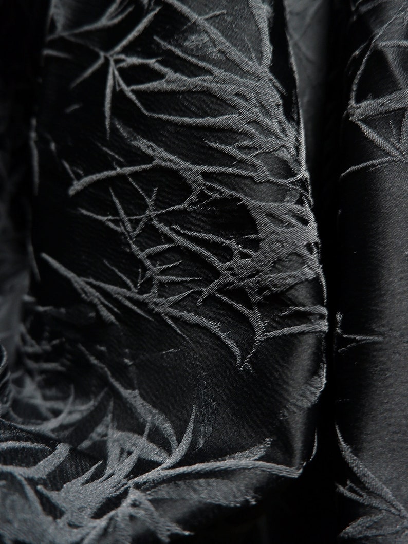 May include: Black fabric with a textured, embossed pattern of leaves and branches. The fabric has a subtle sheen and a soft, drapey feel.