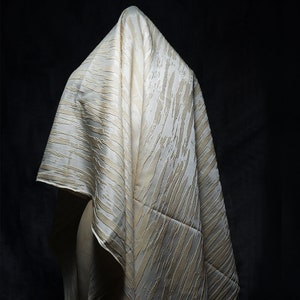 May include: A white and gold patterned fabric draped over a mannequin. The fabric has a subtle sheen and a textured surface.