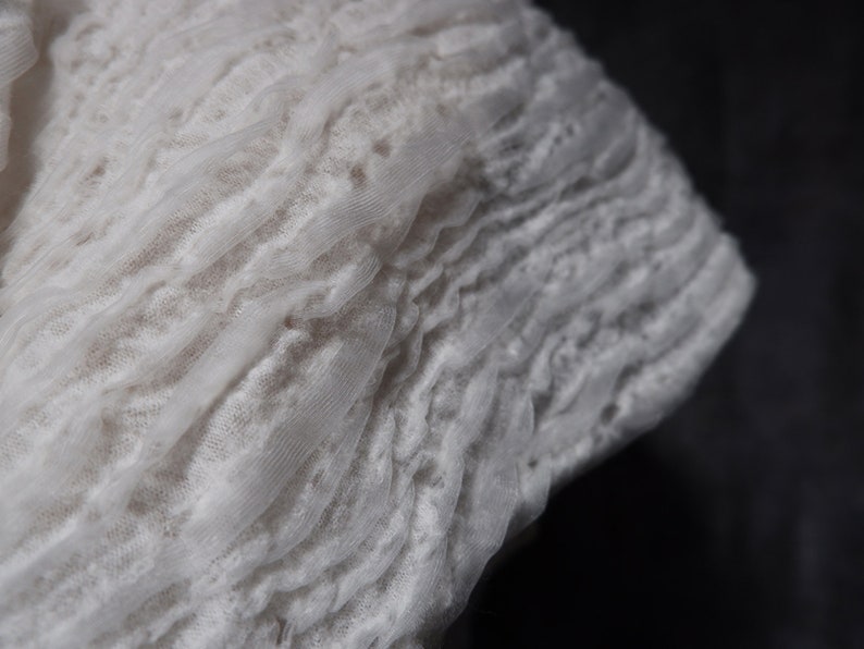 May include: White lace fabric with a ruffled texture. The fabric is soft and delicate, with a subtle sheen.