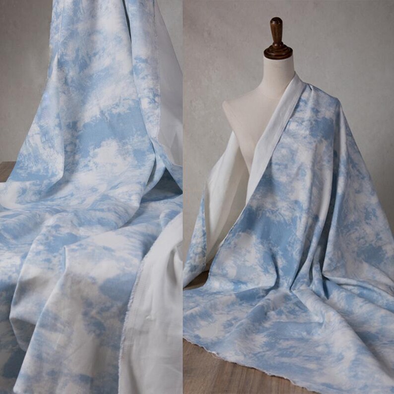 Op de afbeelding: Een lichtblauwe stof met een wit wolkenpatroon. De stof is gevouwen en gedrapeerd over een mannequin.