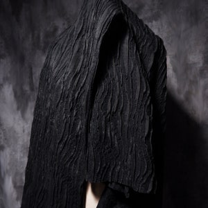 May include: A black textured fabric draped over a person's head and shoulders. The fabric has a wavy, rippled pattern.