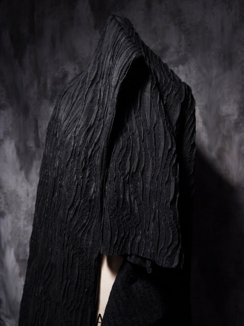 May include: A black textured fabric draped over a person's head and shoulders. The fabric has a wavy, rippled pattern.