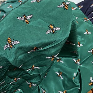 以下が含まれることがあります： 白とオレンジの蜂が繰り返し描かれた緑色の布。布は折り畳まれ、しわくちゃになっている。