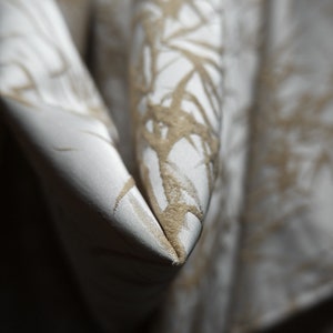 May include: Close-up of a white fabric with a subtle, embossed pattern of brown branches. The fabric is folded in a V-shape, creating a sharp crease.