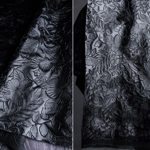 May include: Black fabric with an embossed floral pattern. The fabric has a raised, textured design of flowers and leaves.