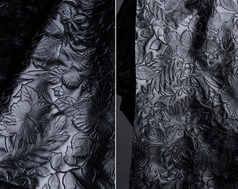 Puede incluir: Tela negra con un patrón floral en relieve. La tela tiene un diseño en relieve de flores y hojas.