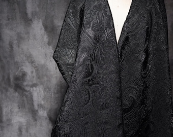 Könnte beinhalten: Schwarze Jacke mit V-Ausschnitt und geprägtem Blumenmuster. Das Kleidungsstück wird auf einer Schaufensterpuppe präsentiert. Der Hintergrund ist eine dunkle, strukturierte Oberfläche.
