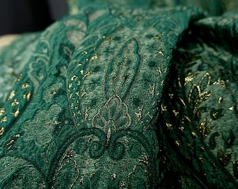 May include: Close-up of a green fabric with a gold paisley pattern. The fabric is soft and luxurious, with a subtle sheen.