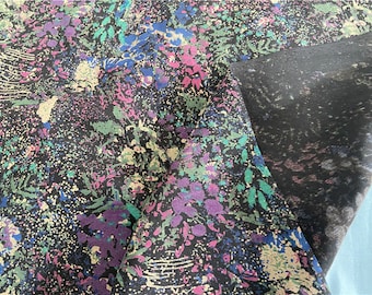 May include: A black fabric with a colorful floral print. The fabric has a dark background with a variety of colors, including pink, blue, green, and yellow. The fabric is folded in half, and the fold is visible in the image.