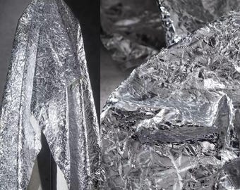 May include: A crumpled silver fabric with a textured surface. The fabric is folded and draped over a surface.