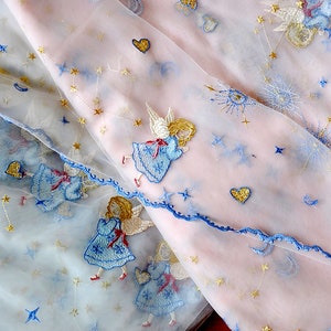 Puede incluir: Tela rosa transparente con bordados azules y dorados de &aacute;ngeles, estrellas y corazones. La tela es delicada y transl&uacute;cida.