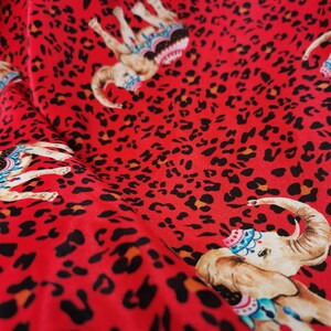 May include: Red fabric with a repeating pattern of black leopard spots and colorful elephants wearing ornate headbands.