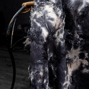 May include: Close-up of a tie-dye fabric with a distressed, fringed edge. The fabric features a pattern of black and white swirls, creating a textured appearance. The fabric is draped over a chair.