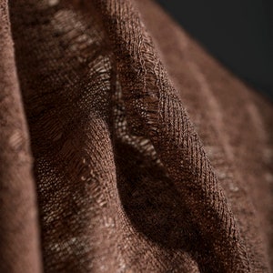 May include: Close-up of a brown fabric with a textured weave. The fabric is folded and has a slightly frayed edge.