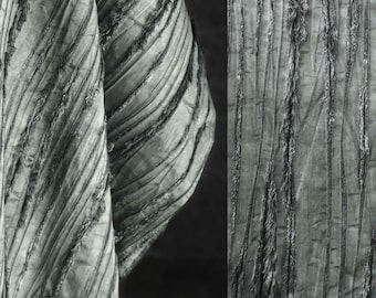 May include: Gray fabric with a textured, striped pattern and frayed edges. The fabric is folded in a triangular shape on the left side of the image and laid flat on the right side.