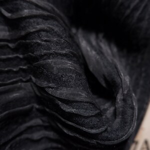 May include: Close-up of black fabric with a crinkled, textured surface. The fabric is folded and draped, creating a soft, flowing look.