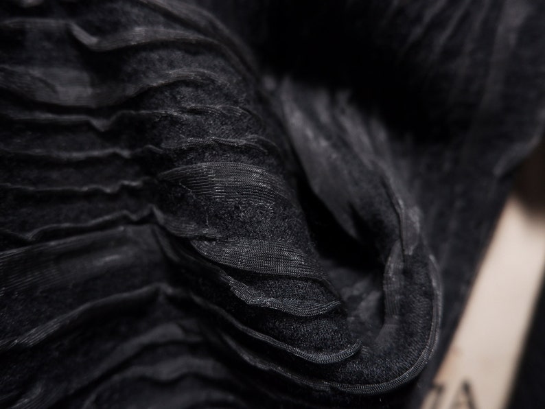 May include: Close-up of black fabric with a crinkled, textured surface. The fabric is folded and draped, creating a soft, flowing look.
