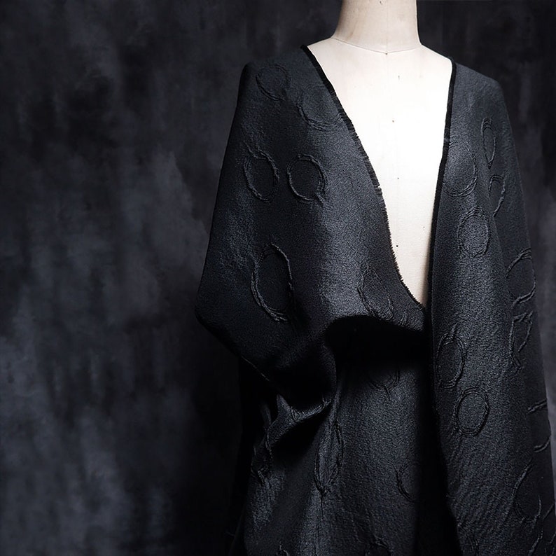 May include: Black fabric with a textured pattern of circles. The fabric is draped over a dress form.
