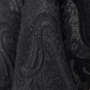 K&ouml;nnte beinhalten: Nahaufnahme eines schwarzen Stoffes mit detailliertem Paisley-Muster. Der Stoff hat eine strukturierte Oberfl&auml;che mit dezentem Glanz, der Tiefe und visuelles Interesse erzeugt. Das Design zeigt wirbelnde, geschwungene Motive.