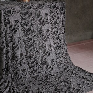 May include: Gray distressed fabric with a textured, ripped, and torn pattern. The fabric is draped over a surface and appears to be a backdrop or stage prop.